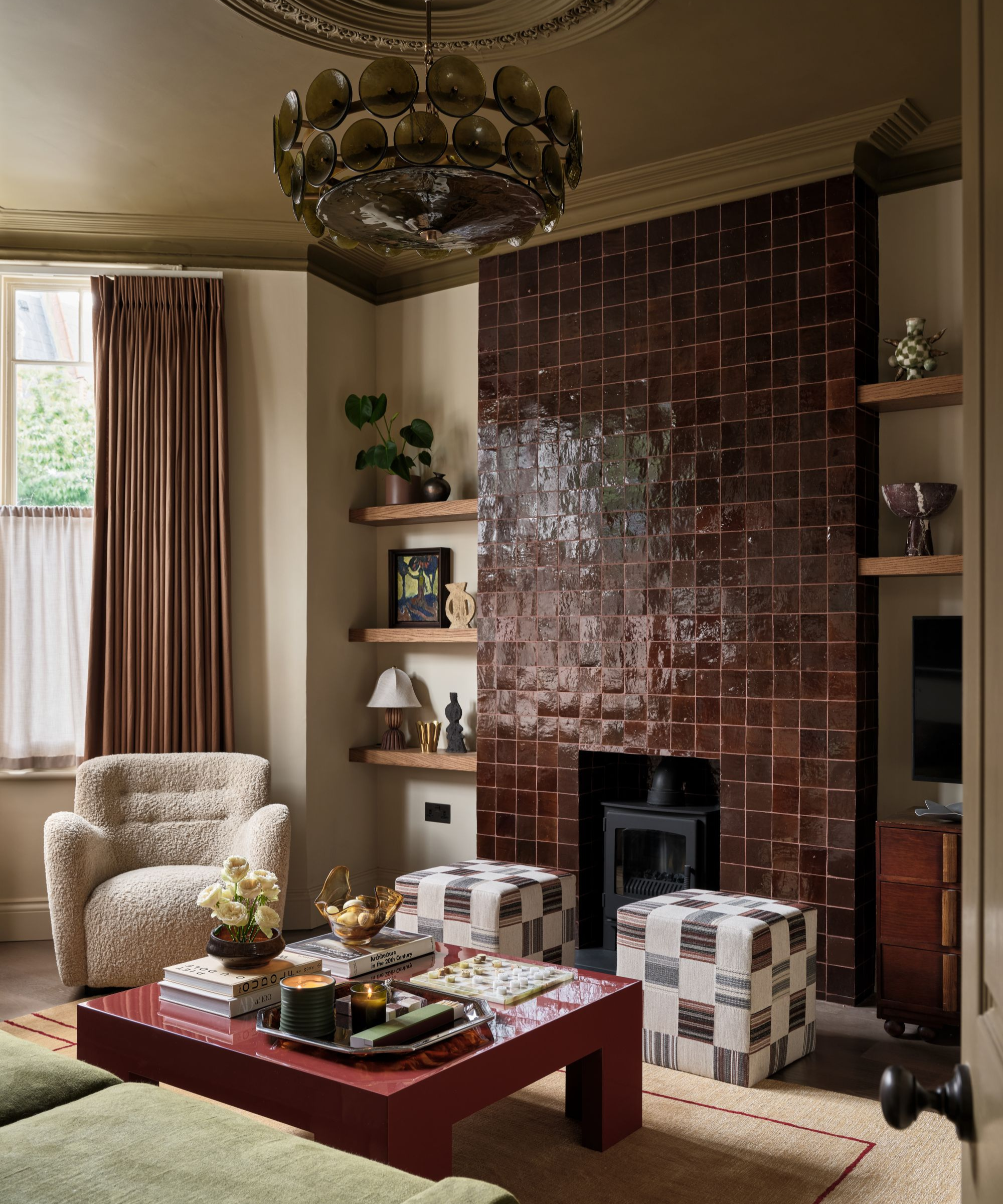 a cozy living room with a zellige tile fireplace, two matching ottomans, a glossy coffee table, a boucle accent chair, and a large glass chandelier