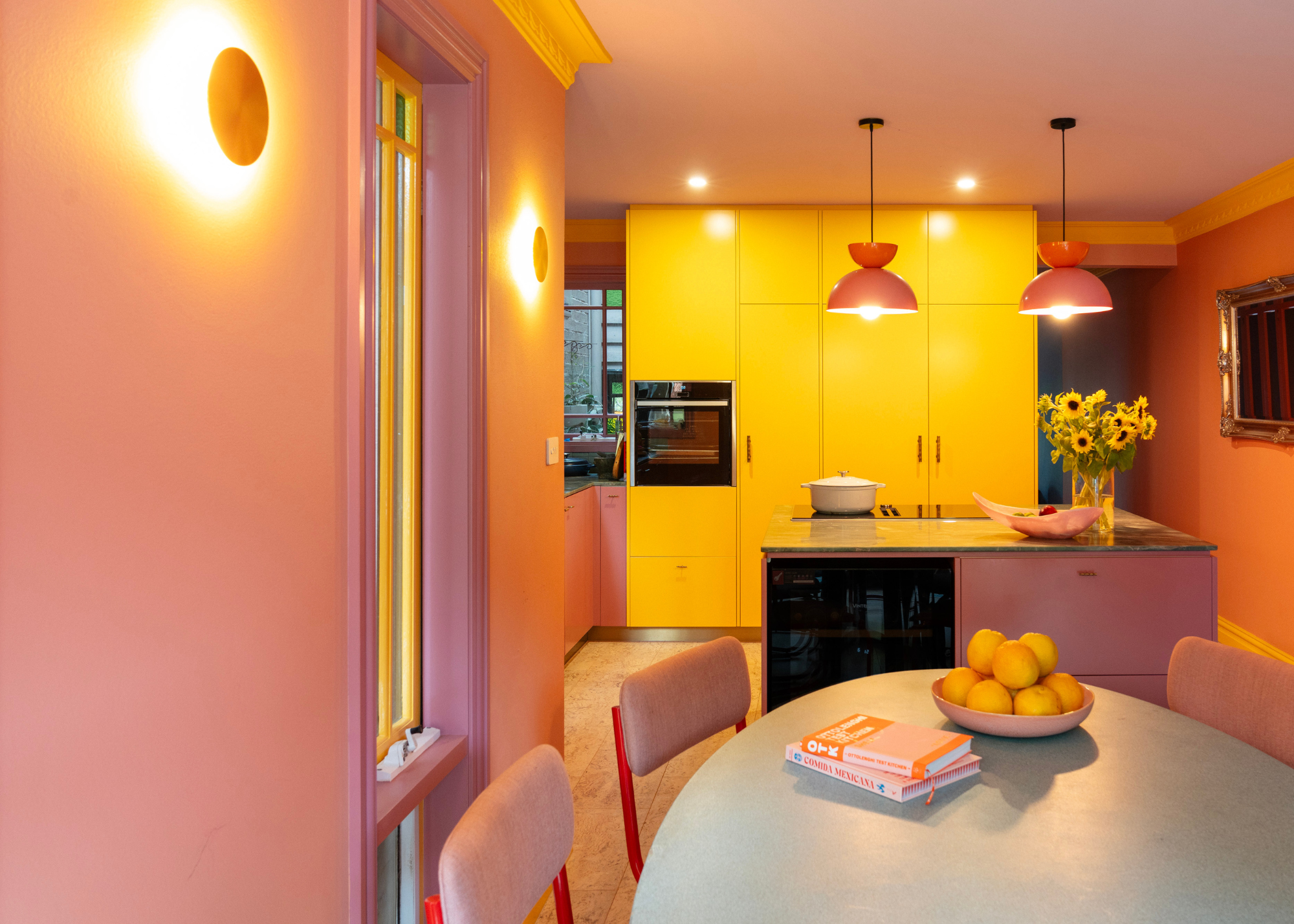 A pastel pink and yellow kitchen with strong lighting and a small kitchen island.