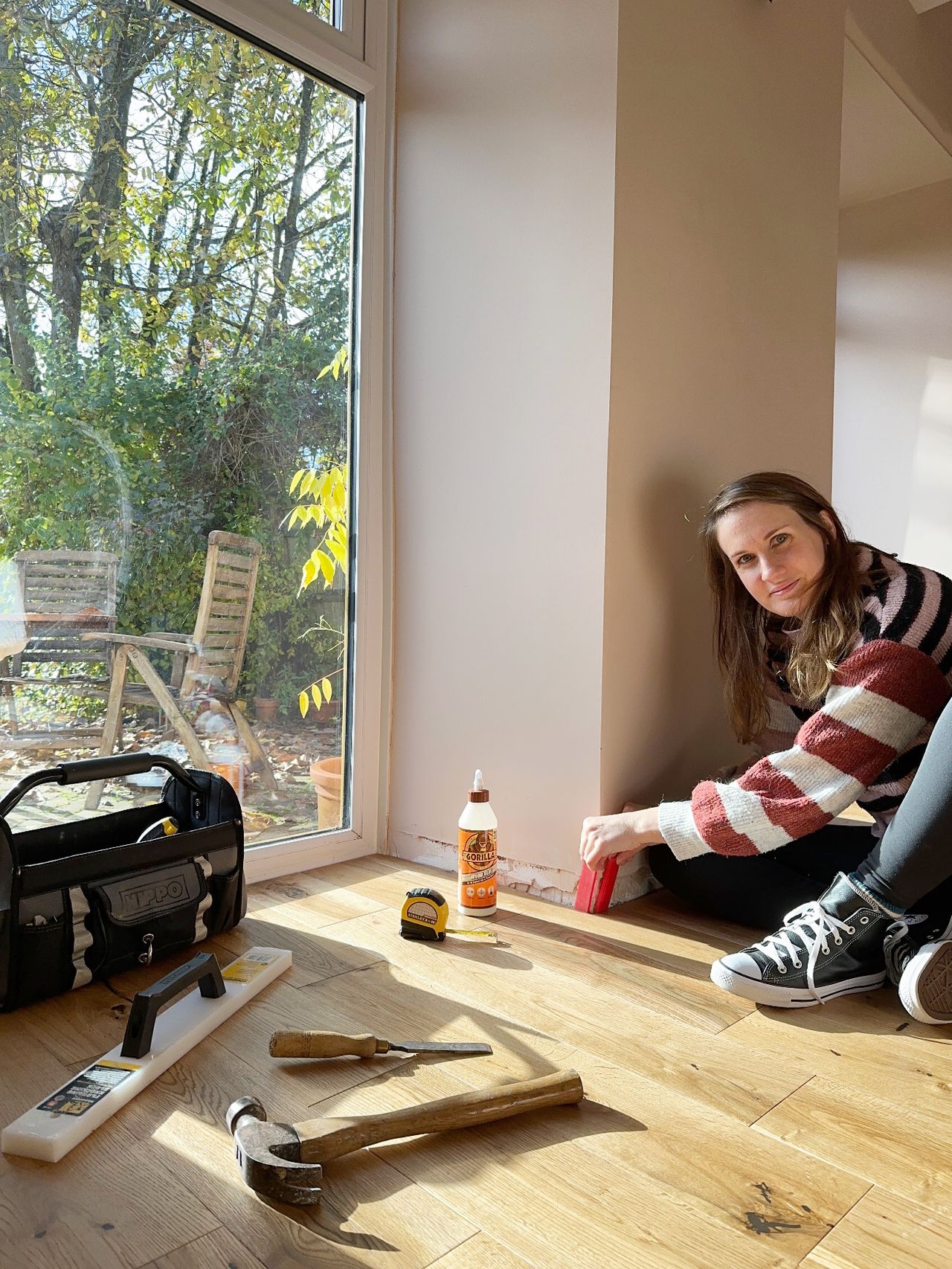 A woman sits on the floor of her home completing a DIY task involving skirting boards and gorilla glue