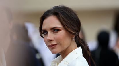 Victoria Beckham smiling for cameras with a white suit on