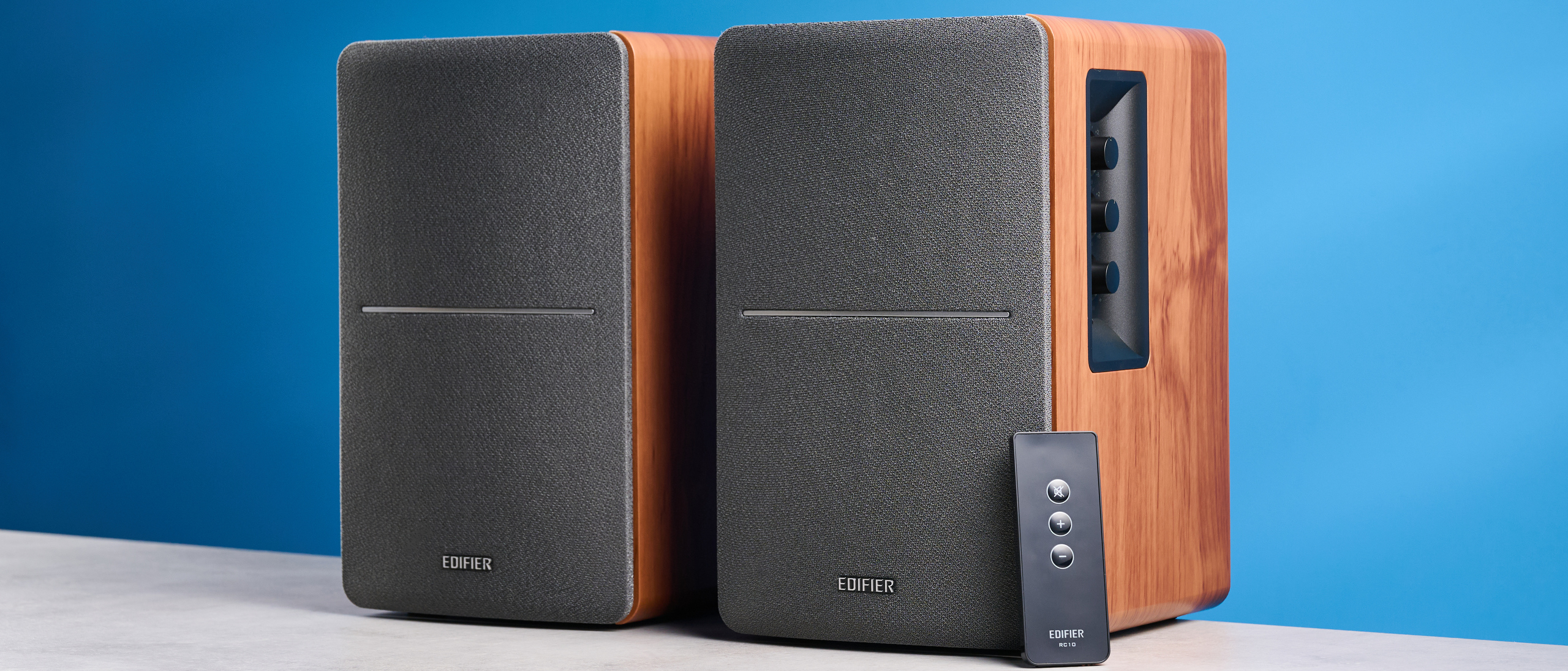 the edifier r1280t bookshelf speakers in wood brown photographed against the blue background, showing the volume adjustment dials, internal drivers and tweeters, RCA and aux inputs, and remote 