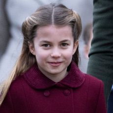 Princess Charlotte wears a red winter coat, Meghan Markle wears a white strapless dress while posing with Prince Harry, who is wearing a tan suit