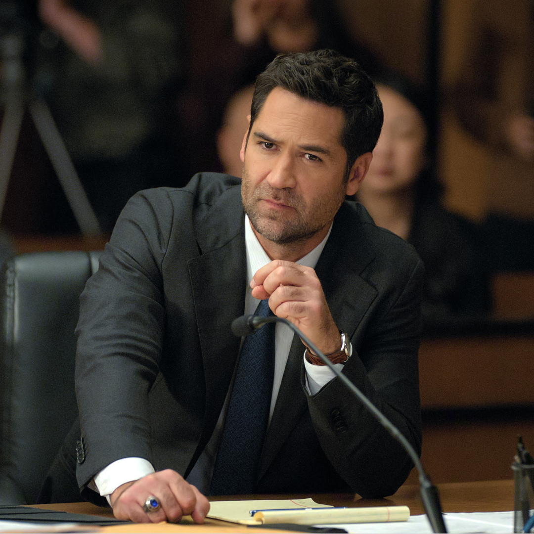Manuel Garcia-Rulfo as mickey heller wearing a suit and talking into a microphone while sitting at a desk in a court room in the lincoln lawyer season 4