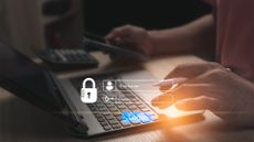 Password security concept image showing person logging into an account on a laptop while using password manager authenticator on smartphone.