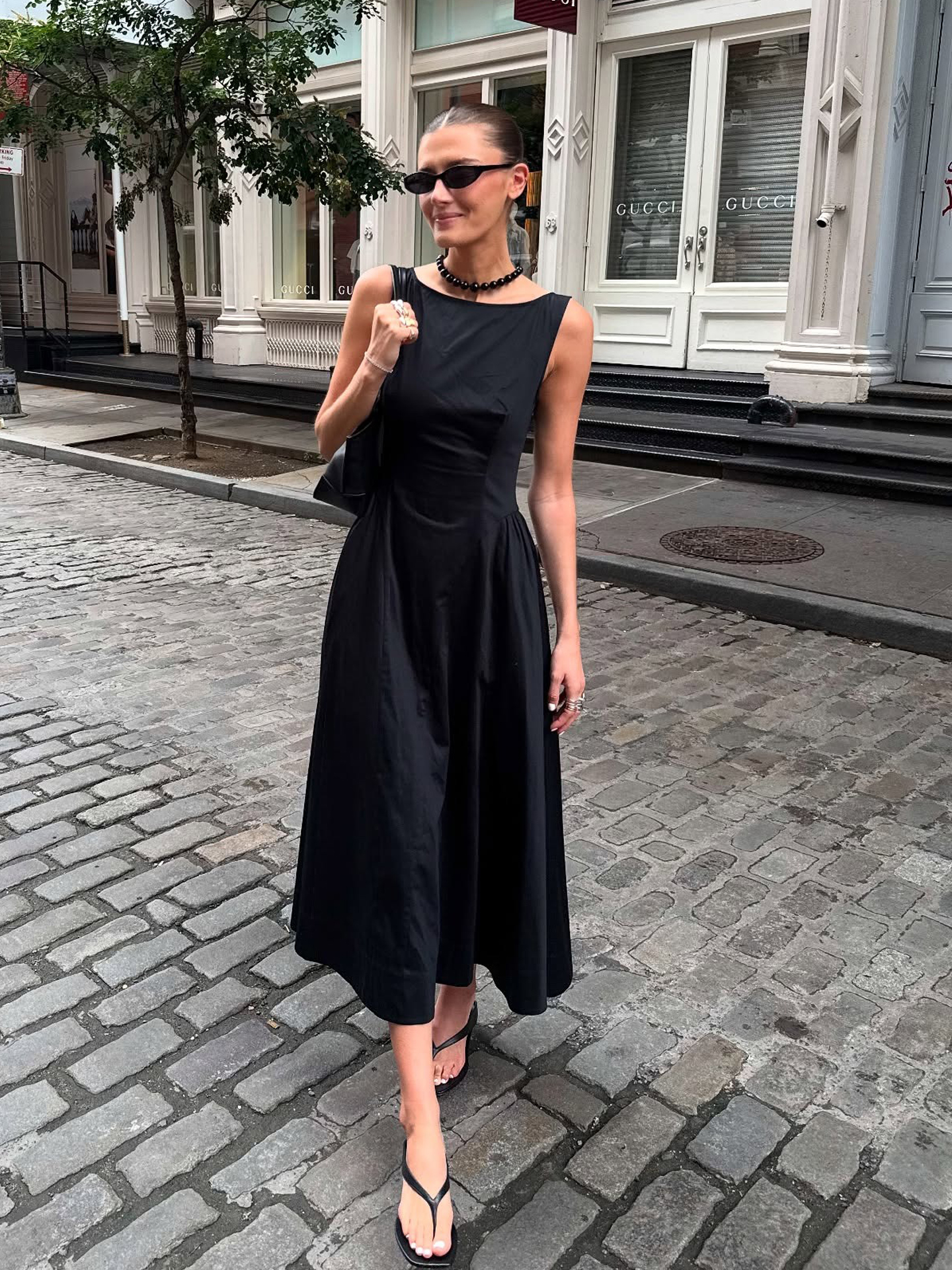 NYC influencer Coco Schiffer wearing a fit and flare black dress with flip-flop sandals