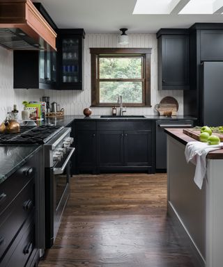 Kitchen with black wall and base cabinetry, hardwood floor, white wall tiles, black marble countertops, gray island, stainless steel handles and faucet