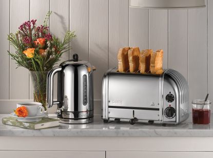 Dualit toaster, one of the best toaster options, and kettle in a kitchen on a worktop with flowers and a cup of tea, in front of a grey wall