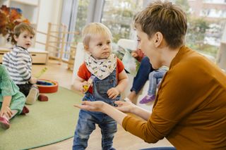 Nursery worker interacting with toddler in a nursery environment while other kids look on