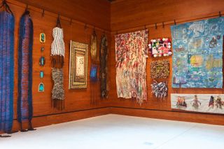 Textile and Fibre Art Programme on display at the Ace Hotel Brooklyn, wooden walls, with colourful artwork hung from black pegs on a wooden rail around the edge of the wall, white floor