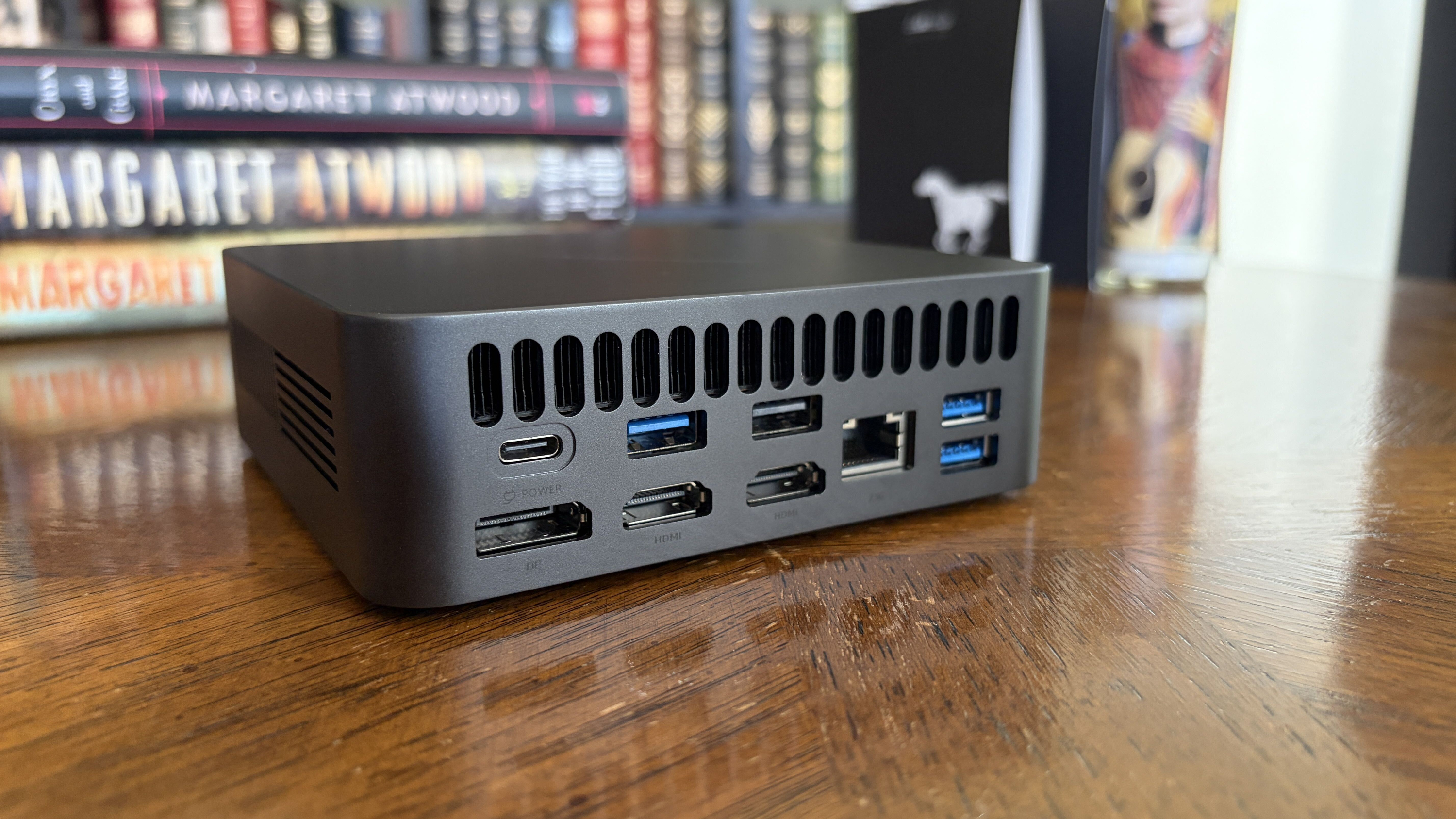 Small black Chuwi mini PC with multiple ports on a wooden surface with books in the background.