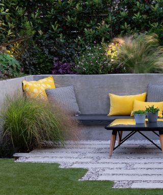 Decked backyard area with grey outdoor sofa, yellow cushions and large planters filled with grasses