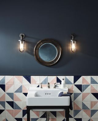 A navy bathroom with a white sink in front of colored wall tiles in blue, pink and white