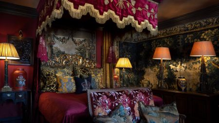 A dramatic red canopied bed surrounded by tapestries and shaded lamps and velvet accents in a room at The Witchery in Edinburgh