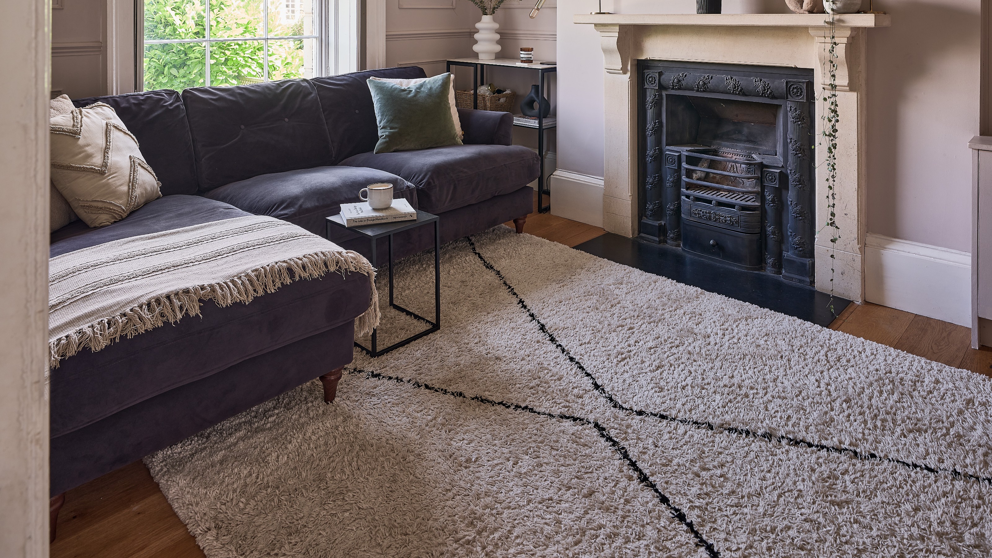 A pink living room with a dark blue chaise sofa on top of a berber-style rug