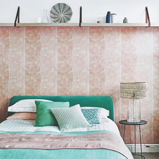 A light bedroom with a pink wallpaper and a glass and rattan table lamp on the small bedside table