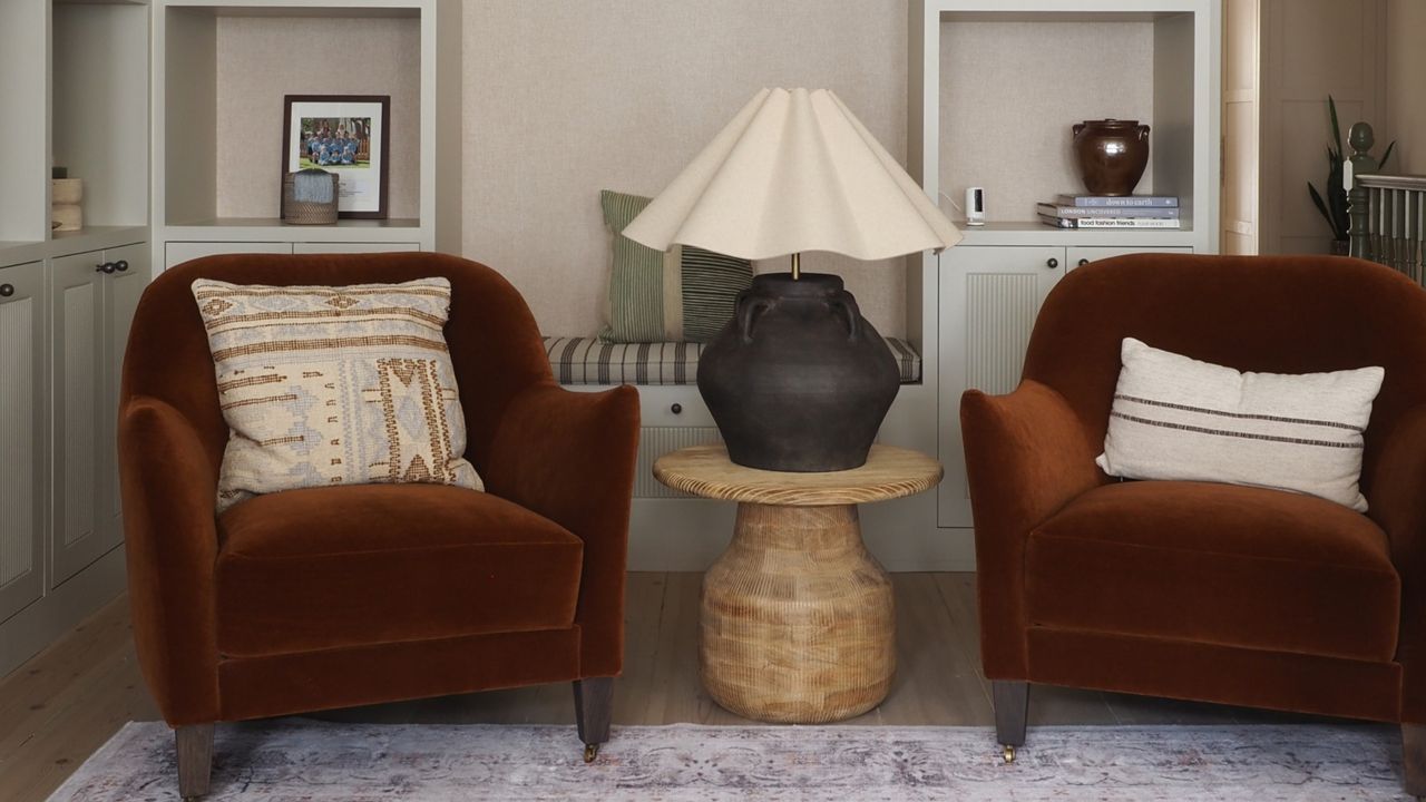 two rust colored accent chairs with a side table in between and a large table lamp