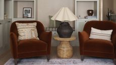 two rust colored accent chairs with a side table in between and a large table lamp