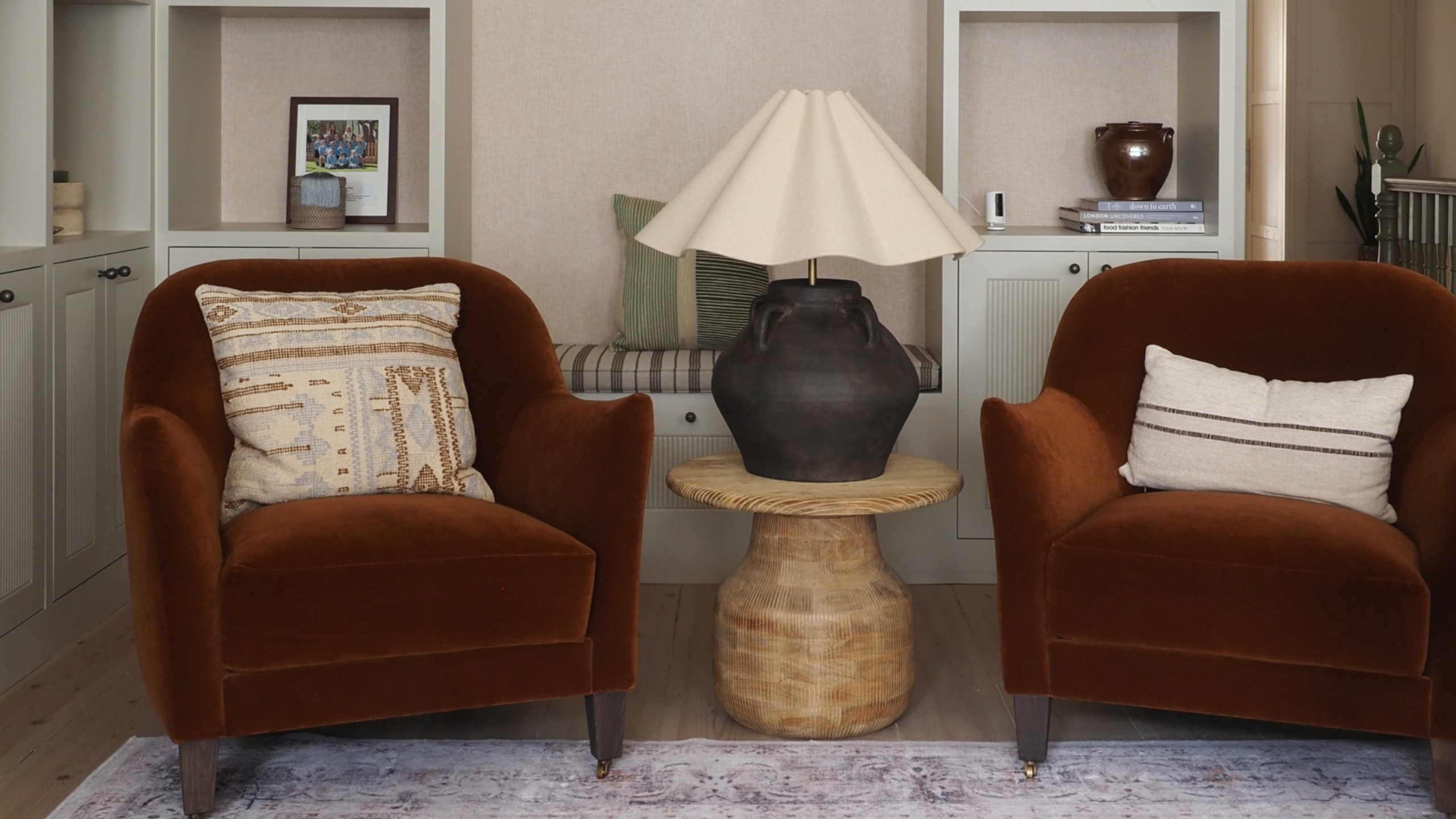 two rust colored accent chairs with a side table in between and a large table lamp