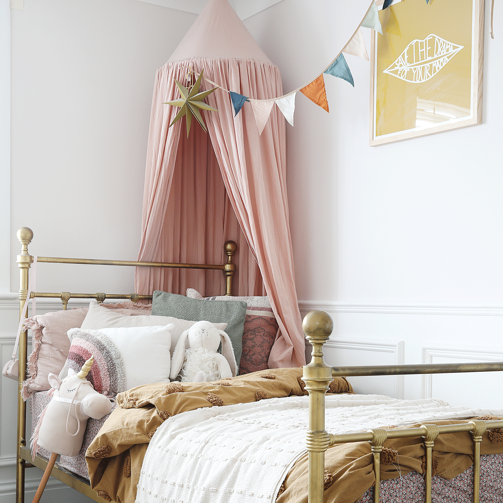 a child's bedroom with a gold wrought iron bed and a pink canopy and colourful bunting over the bed