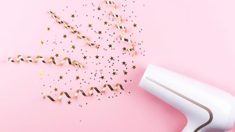 Hairdryer on a pink background with curly streamers and confetti
