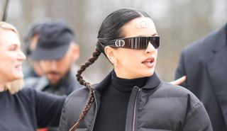Rosalia wears Dior sunglasses, earrings, a black turtleneck pullover , a black cropped winter puffer jacket , outside Dior, during the Womenswear Fall/Winter 2024/2025 as part of Paris Fashion Week on February 27, 2024 in Paris, France.