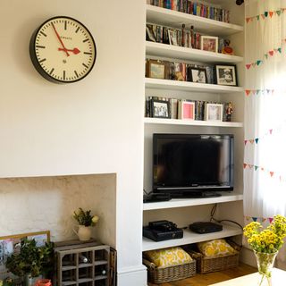 living room with white wall and shelving with books and clock on wall