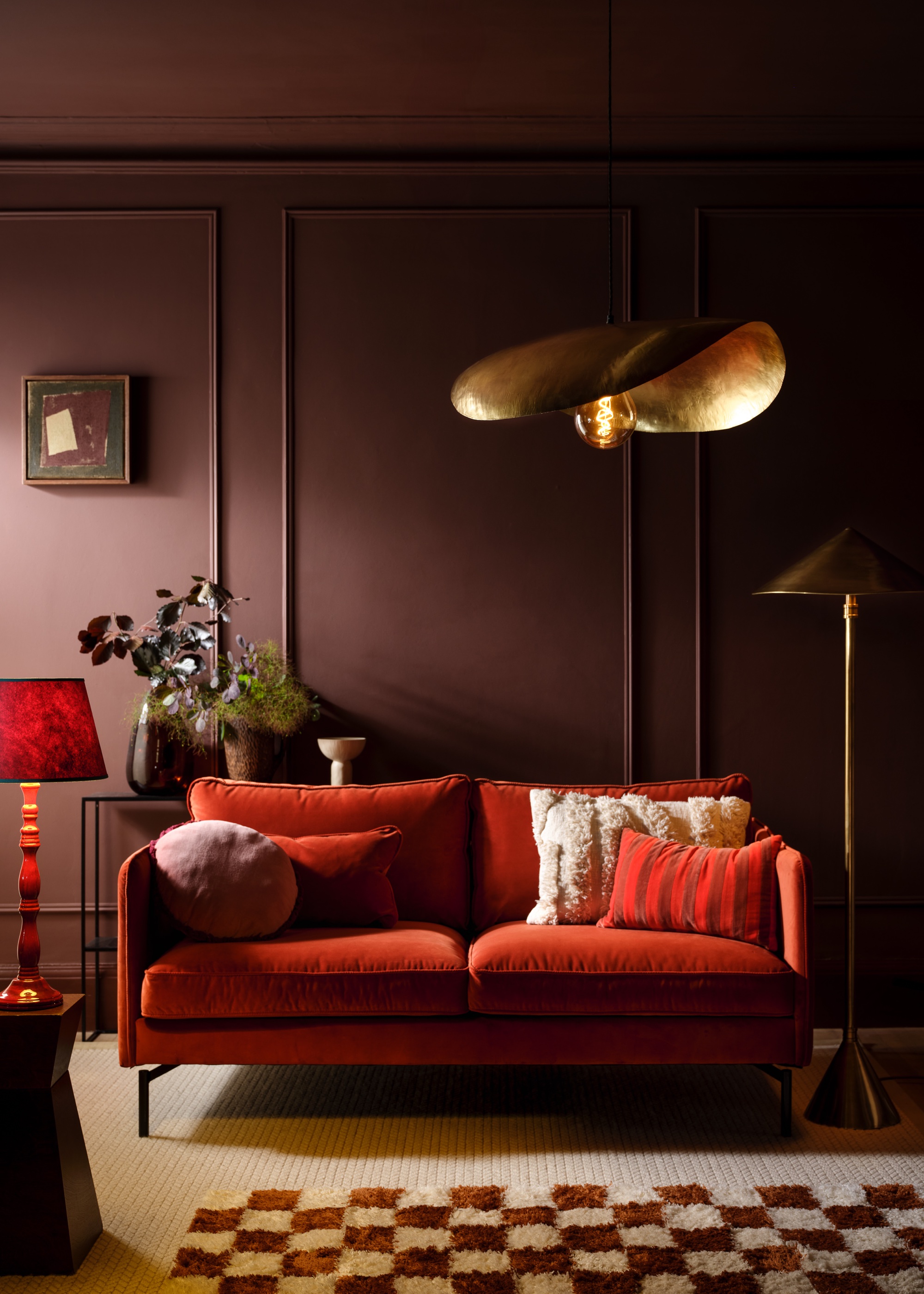 burgundy wall paneling with red sofa, checked rug and brass lighting fixtures