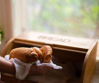 A wooden bread box with pastries being placed into it