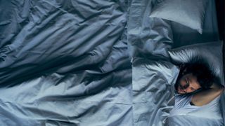 A man lies awake at night. He is lying on his back in a bed with white bedding. 