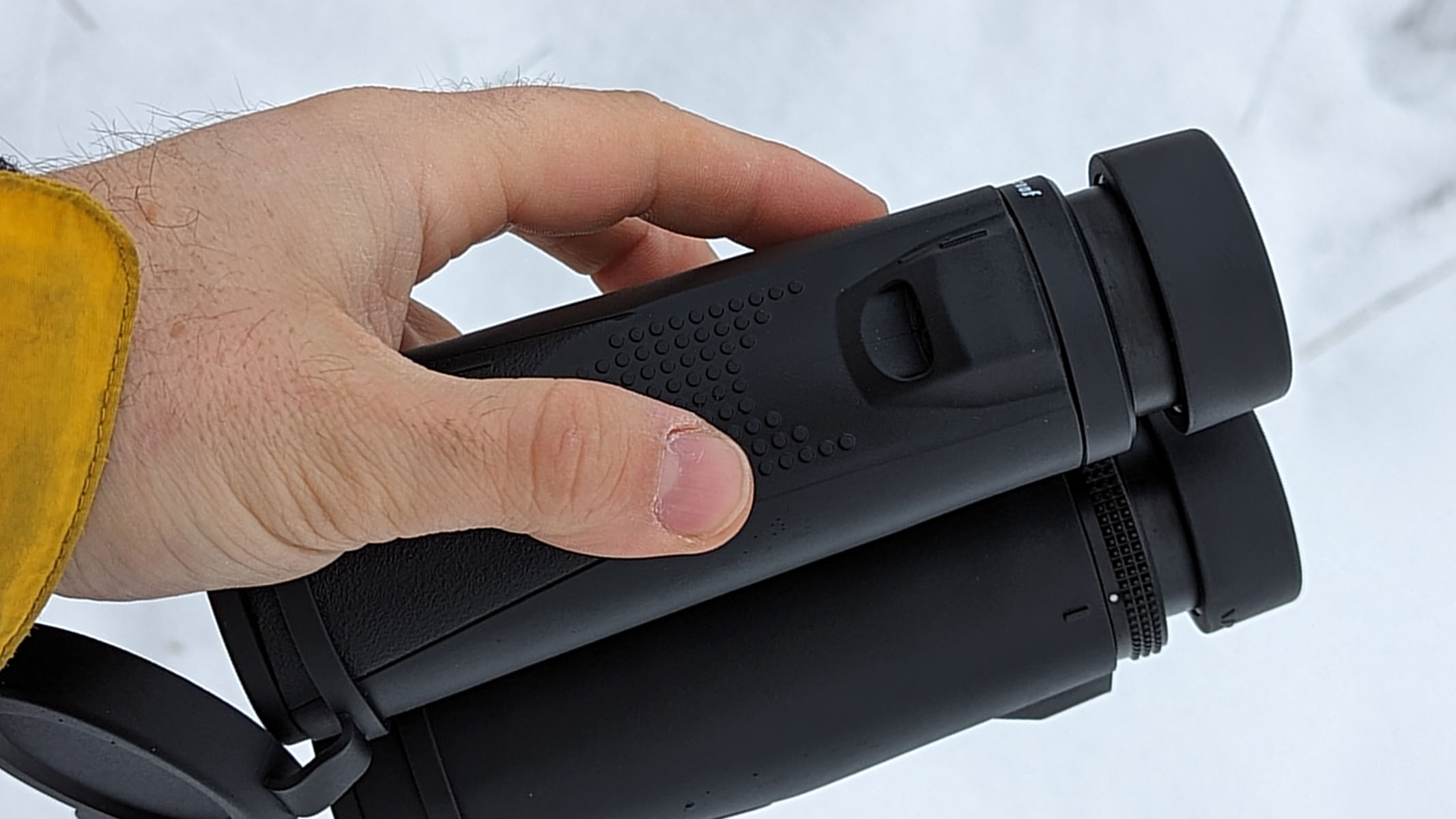 The textured grip on the side of the binoculars can be seen set against a snowy backdrop