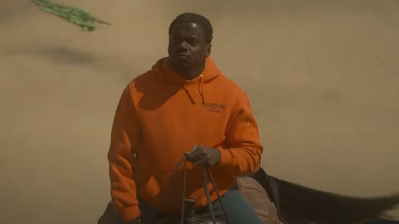 Daniel Kaluuya wearing an orange sweatshirt while riding a horse in Nope