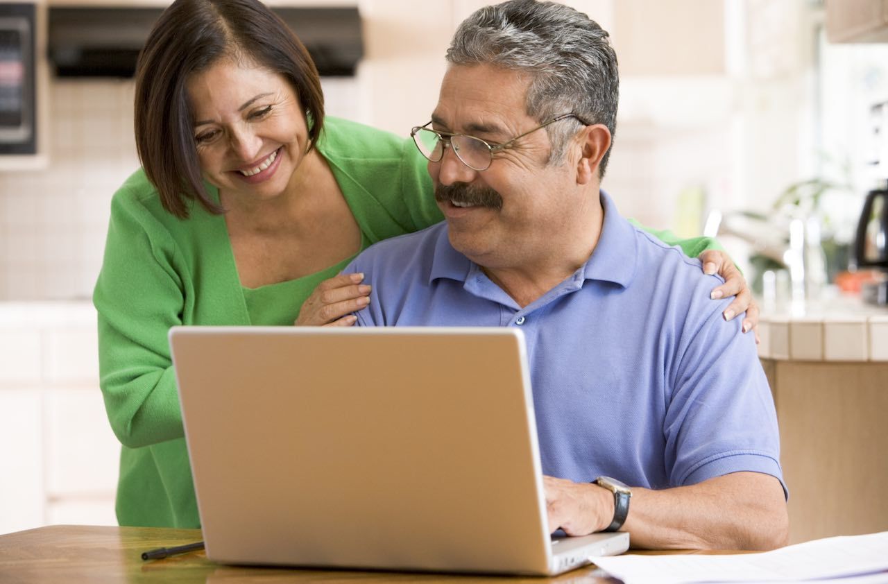 Couple in kitchen with laptop smiling