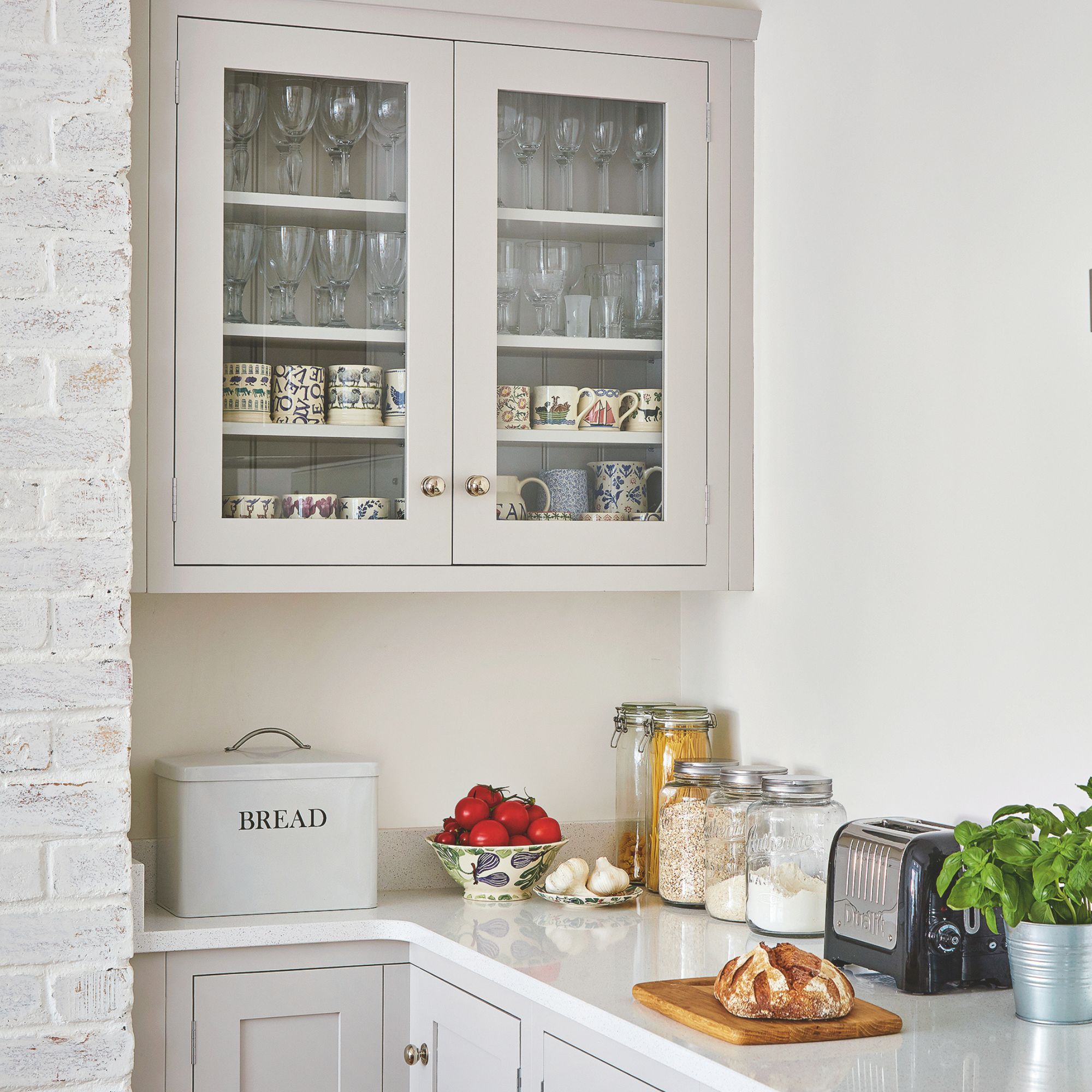 Kitchen with a upper cabinet filled with glasses and mugs, and lots of food items on the kitchen worktop