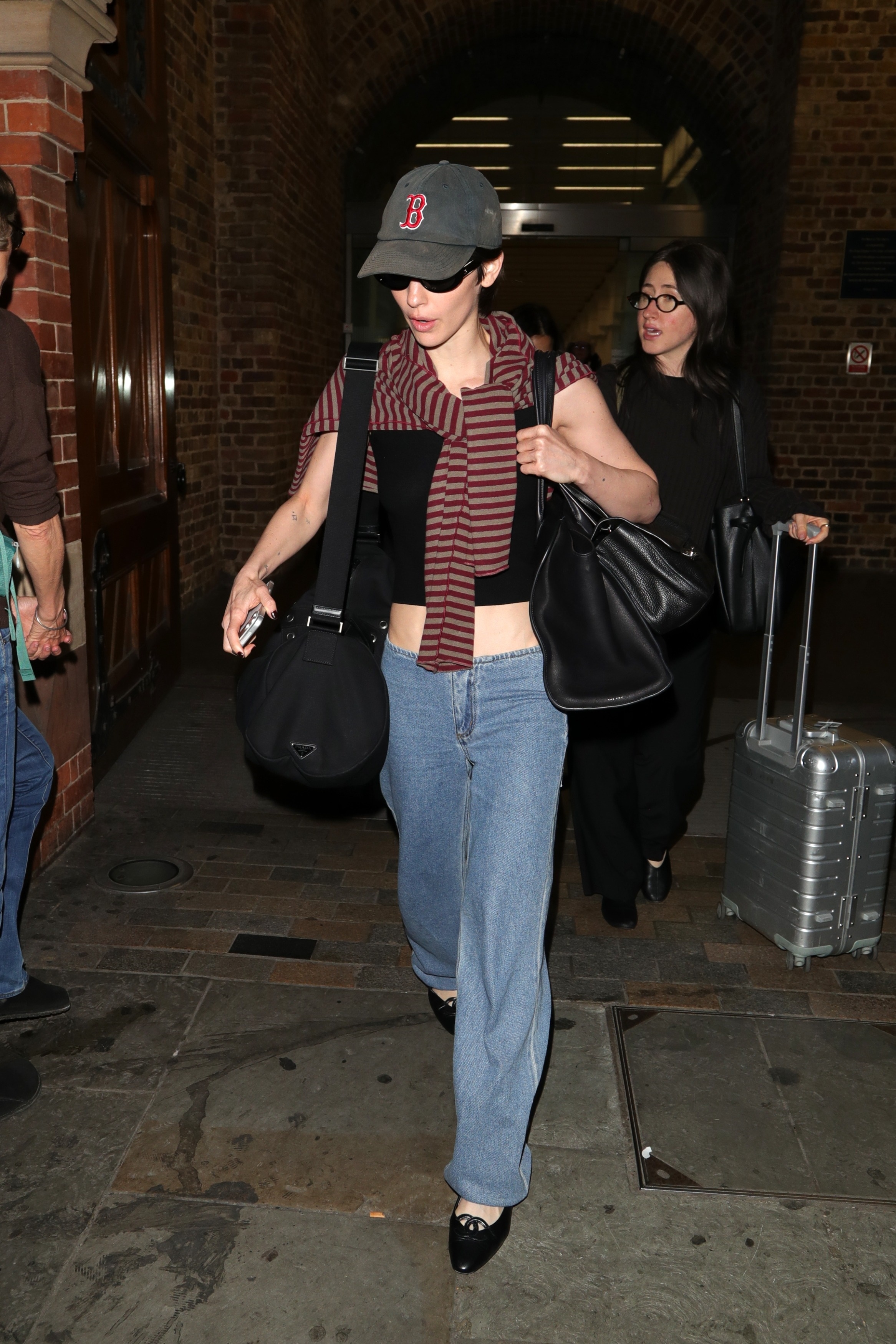 Gracie Abrams wears a Boston hat, a striped sweater, a black tank, Still Here Sport Jeans, and black ballet flats.