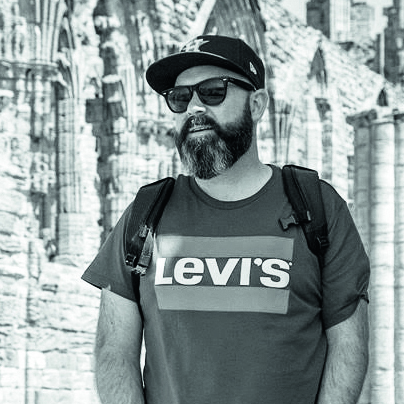 A person wearing a Levi&#039;s t-shirt and a cap stands in front of an old stone structure, exuding a casual, urban vibe