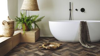 Neutral bathroom with herringbone wood effect flooring with a white oval-shaped freestanding bath