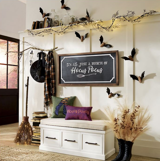 An entryway with a storage bench, an overhead shelf, and witch themed Halloween decorations