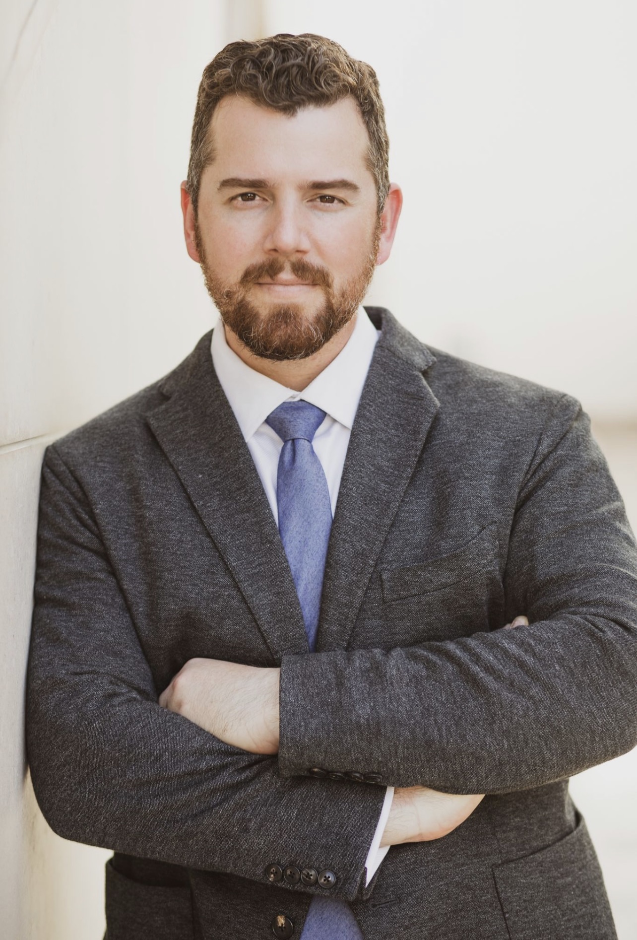 a white man in a gray suit with a blue tie and brown beard