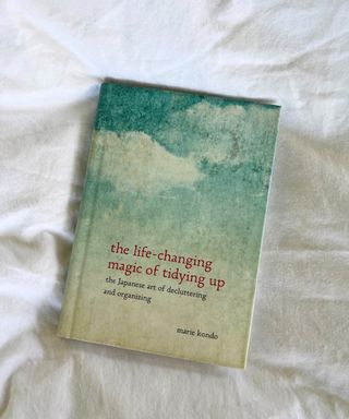 A hardback blue copy of the life-changing magic of tidying up with red text on white bedsheets