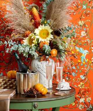 Easy Thanksgiving decor ideas. Table decorated with colorful base of flowers, orange patterned wallpaper.