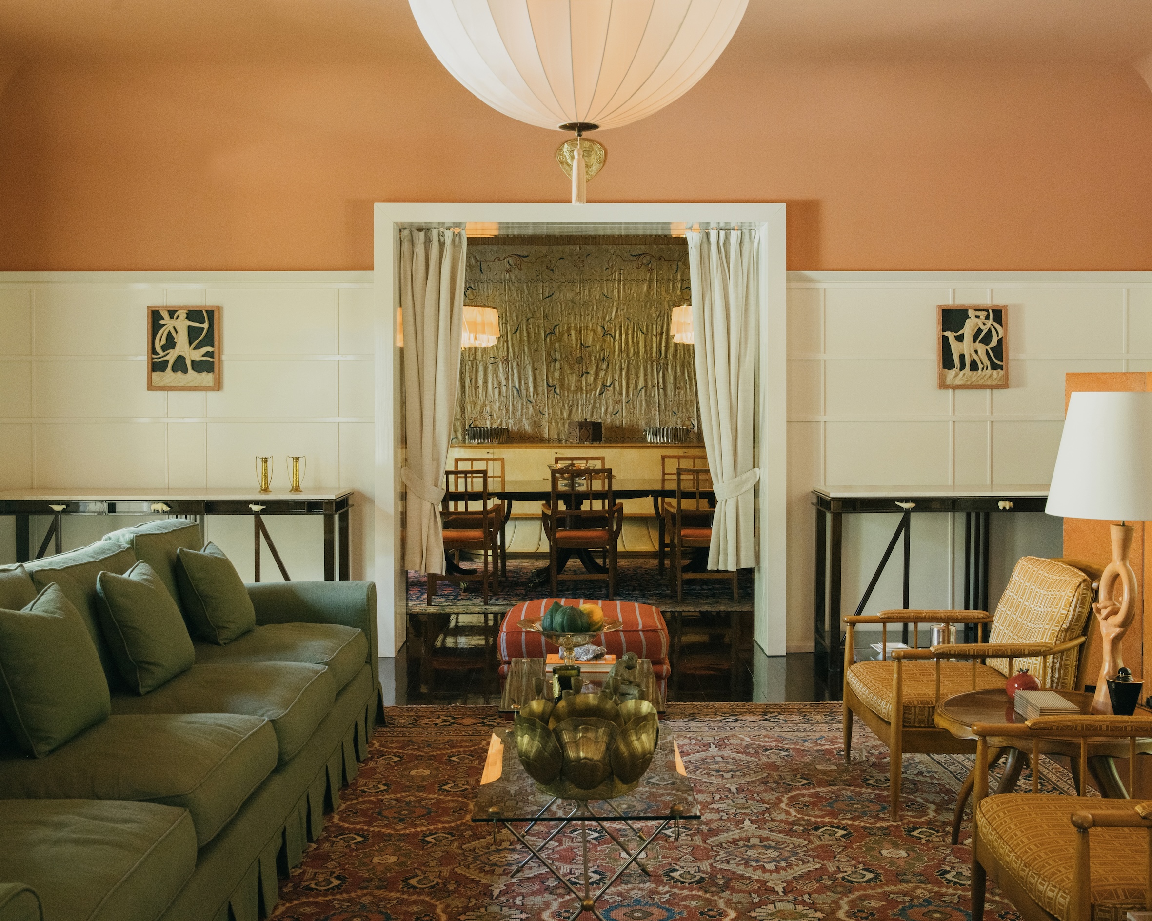 A salmon-hued, palatial living room is filled with antique and vintage furniture, carpets, and plush textiles.