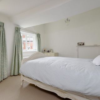 a light coloured bedroom with pale duck-egg patterned curtains and a light cream bed with a blue and white striped duvet cover
