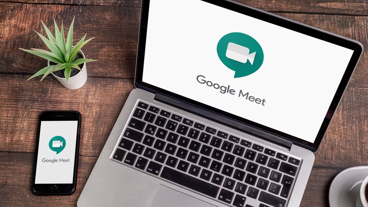 Google Meet logo being displayed on a laptop and a phone that are resting on a wooden table