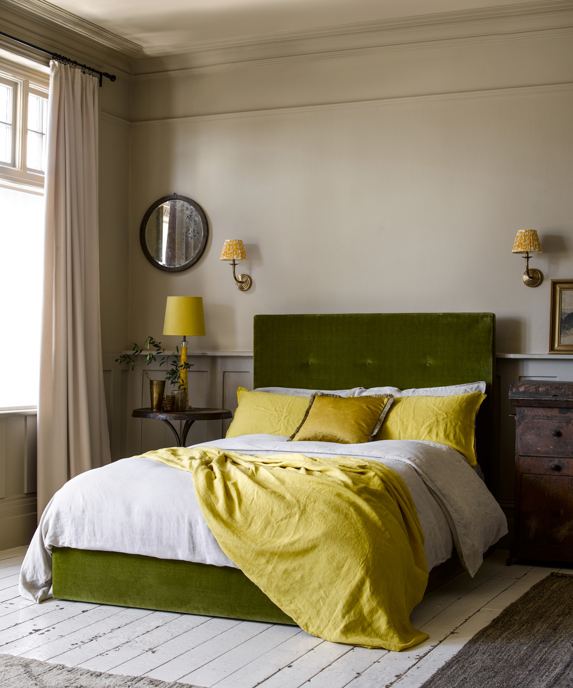 A green velvet bed with yellow and white bedding in front of two wall lamps