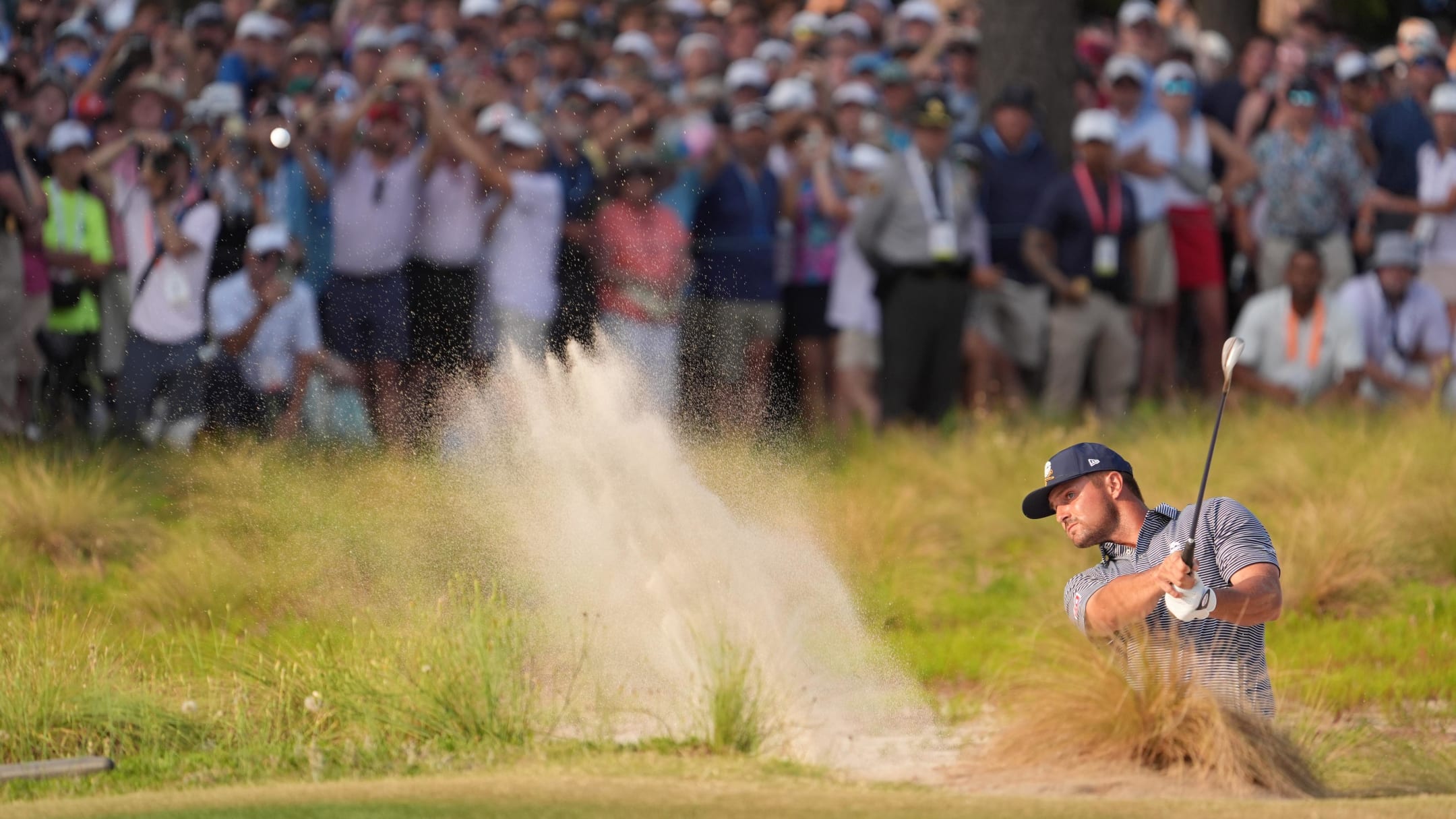 Bryson DeChambeau blasts out of a bunker on the 18th hole during the 2024 US Open 