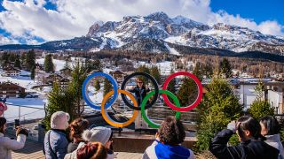 The Olympics 2026 Rings outside of the Olympic village in Cortina with the beautiful mountains and a blue sky in the background.