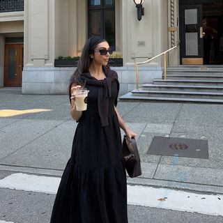 Woman wearing a black dress and holding a coffee on a city street