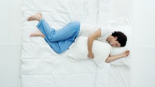 A man lies on a bed in a side sleeping position, holding a pillow to his chest