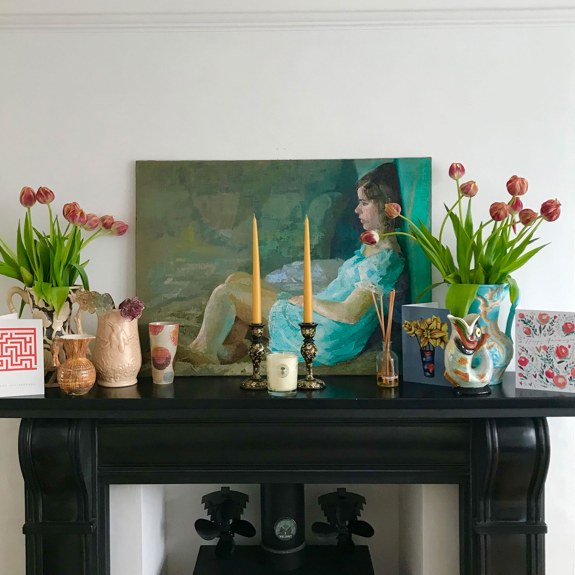 Fireplace mantlepiece with portrait of a girl and displaying candlesticks, cards and vases of tulips