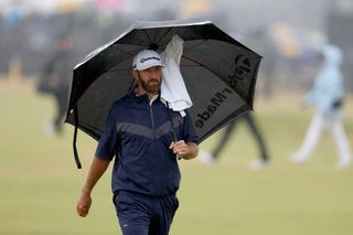 Dustin Johnson walks under an umbrella